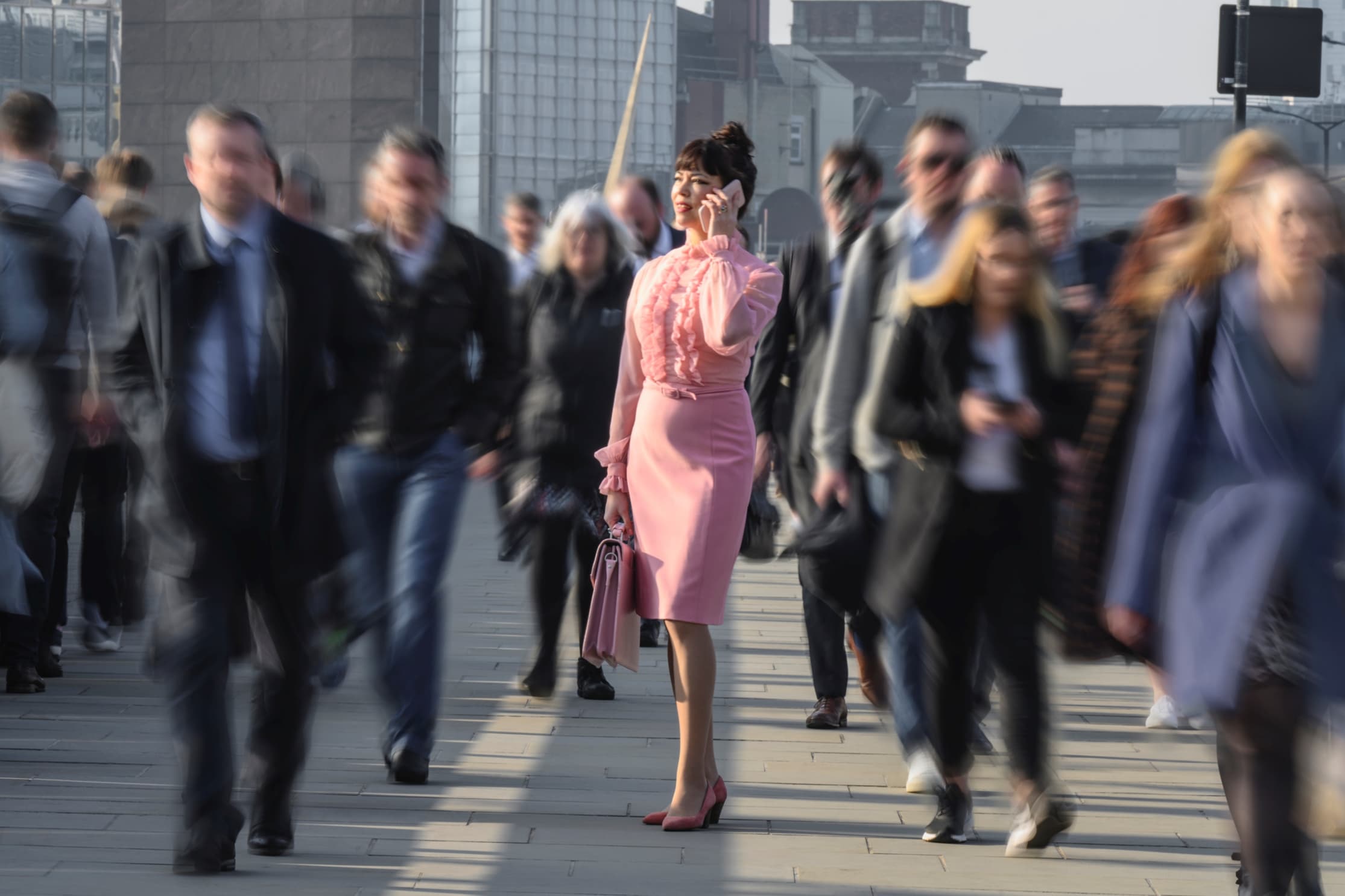 an image of people in city with a lady in pink talking over mobile phone in focus